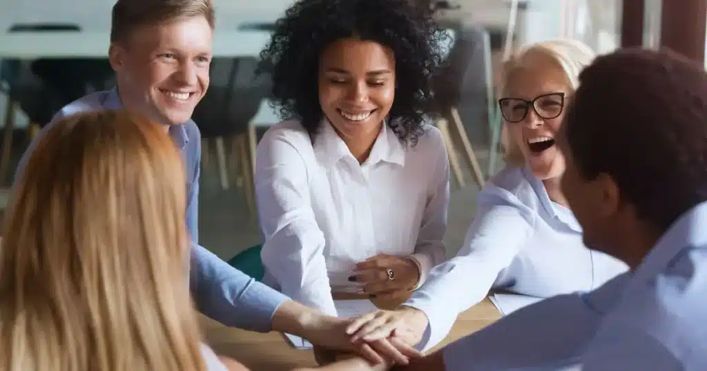 Diverse group of professionals smiling and stacking hands in a team-building activity.